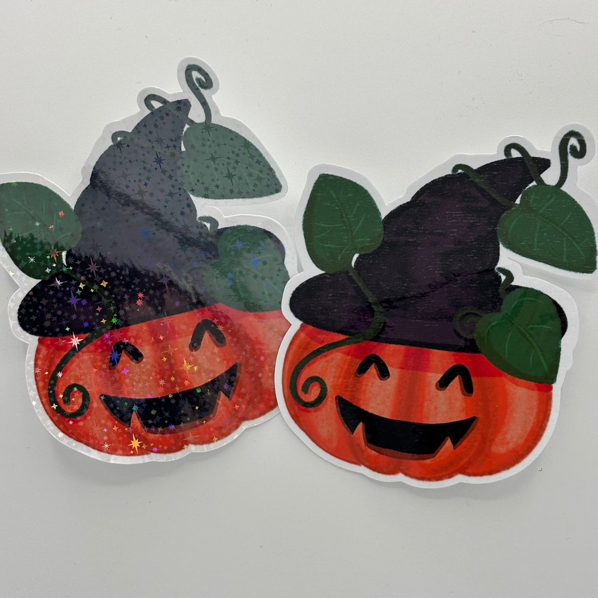 Two Halloween pumpkin stickers with black witch hats, shown side by side on a plain light gray background.