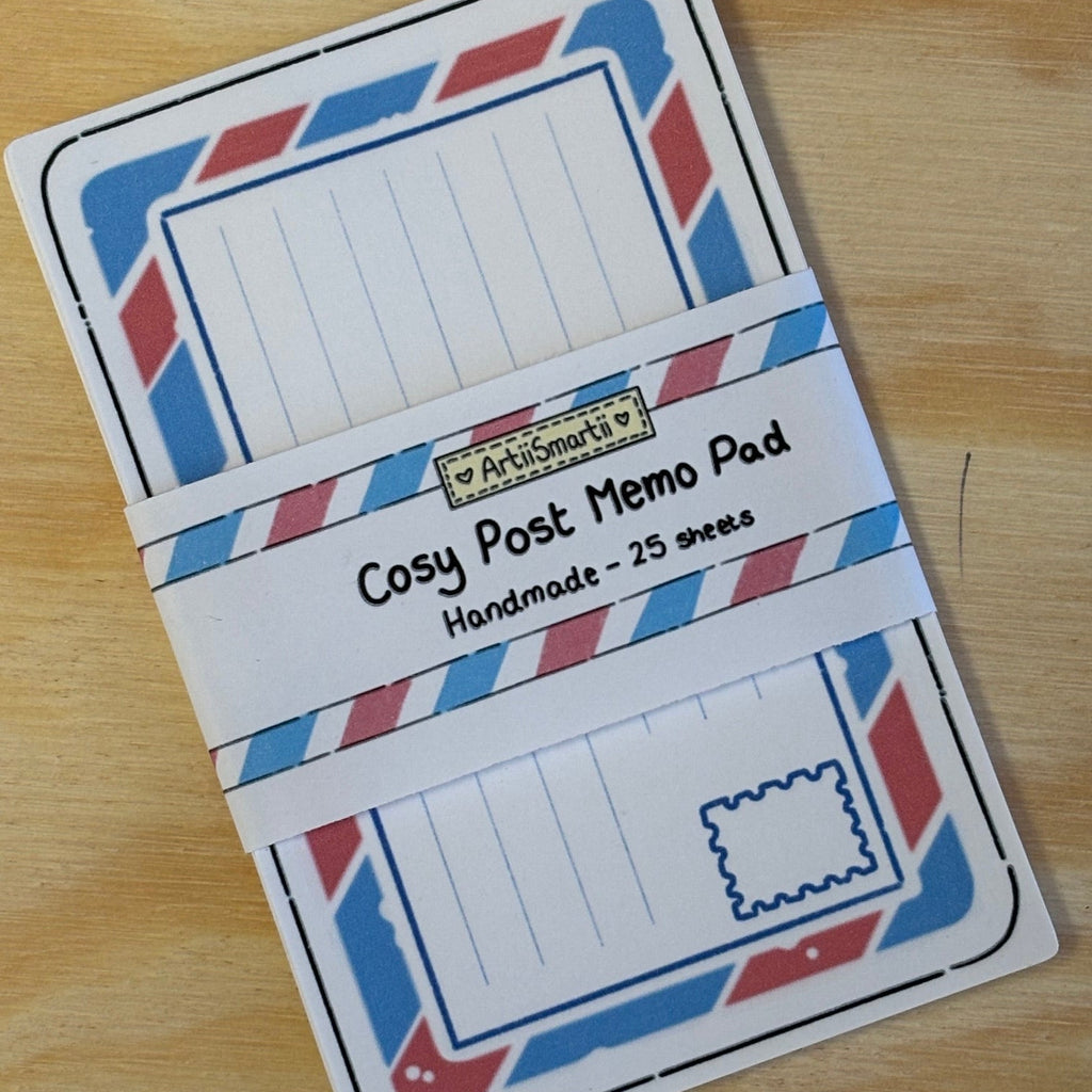 A post memo pad with a retro airmail-style border in red, white, and blue, wrapped in a paper band labeled 'Cosy Post Memo Pad'.