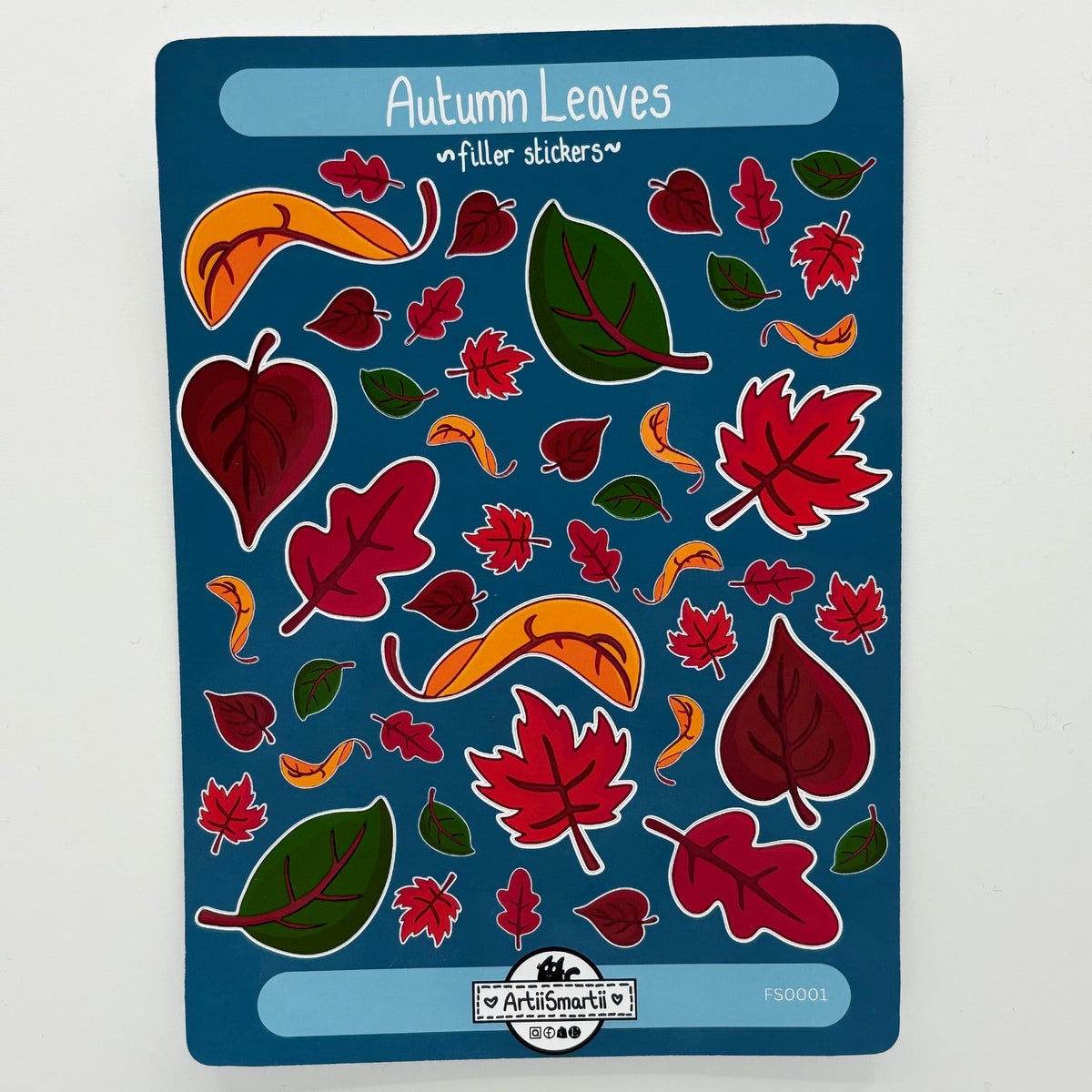 A sheet of 'Autumn Leaves' filler stickers by Art Smarts, featuring various red, green, and orange leaf shapes on a dark blue backing card, photographed flat on a white surface.