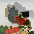A set of autumn-themed paper cutout signs featuring illustrated pumpkins and gourds in red, green, and orange on a beige background, arranged on a white surface.