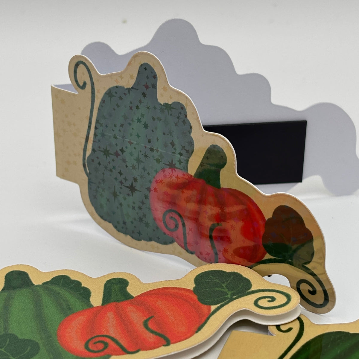A set of autumn-themed paper cutout signs featuring illustrated pumpkins and gourds in red, green, and orange on a beige background, arranged on a white surface.