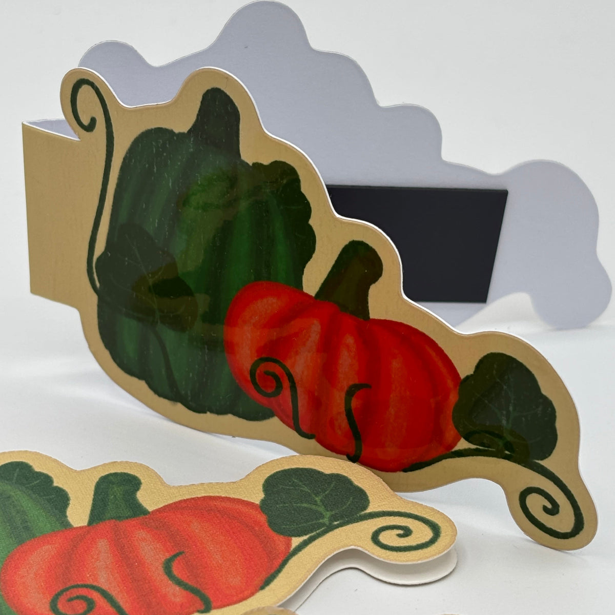 A set of autumn-themed paper cutout signs featuring painted red pumpkins, green vines, and a tan border, arranged on a white surface.