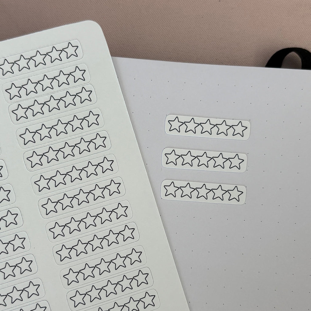 Star-shaped planner stickers shown on a sheet and applied to a white dot-grid notebook page.