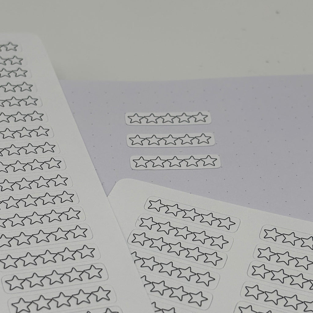 Several sheets of small outlined star stickers arranged on a pale lavender surface against a light gray background.