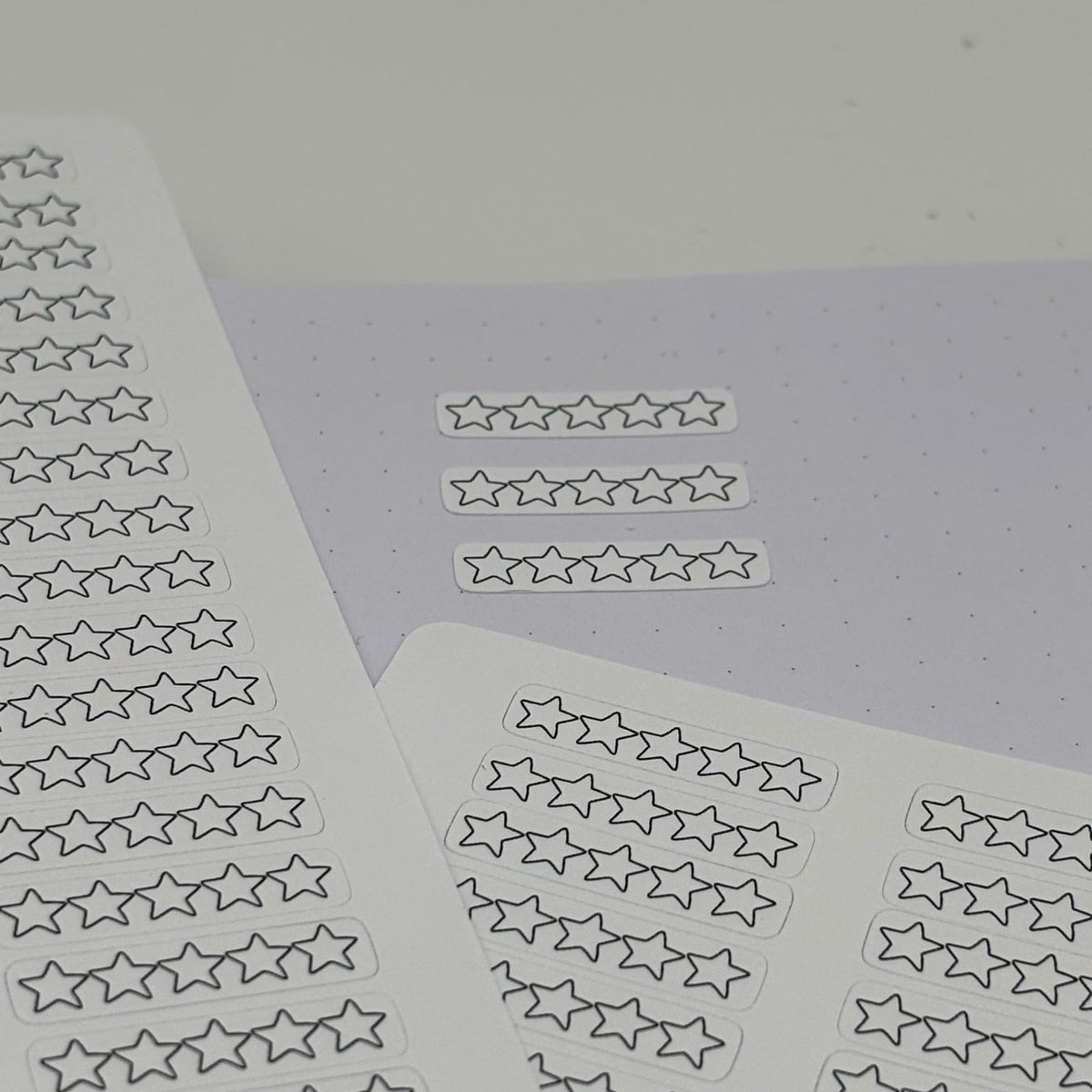 Several sheets of small outlined star stickers arranged on a pale lavender surface against a light gray background.