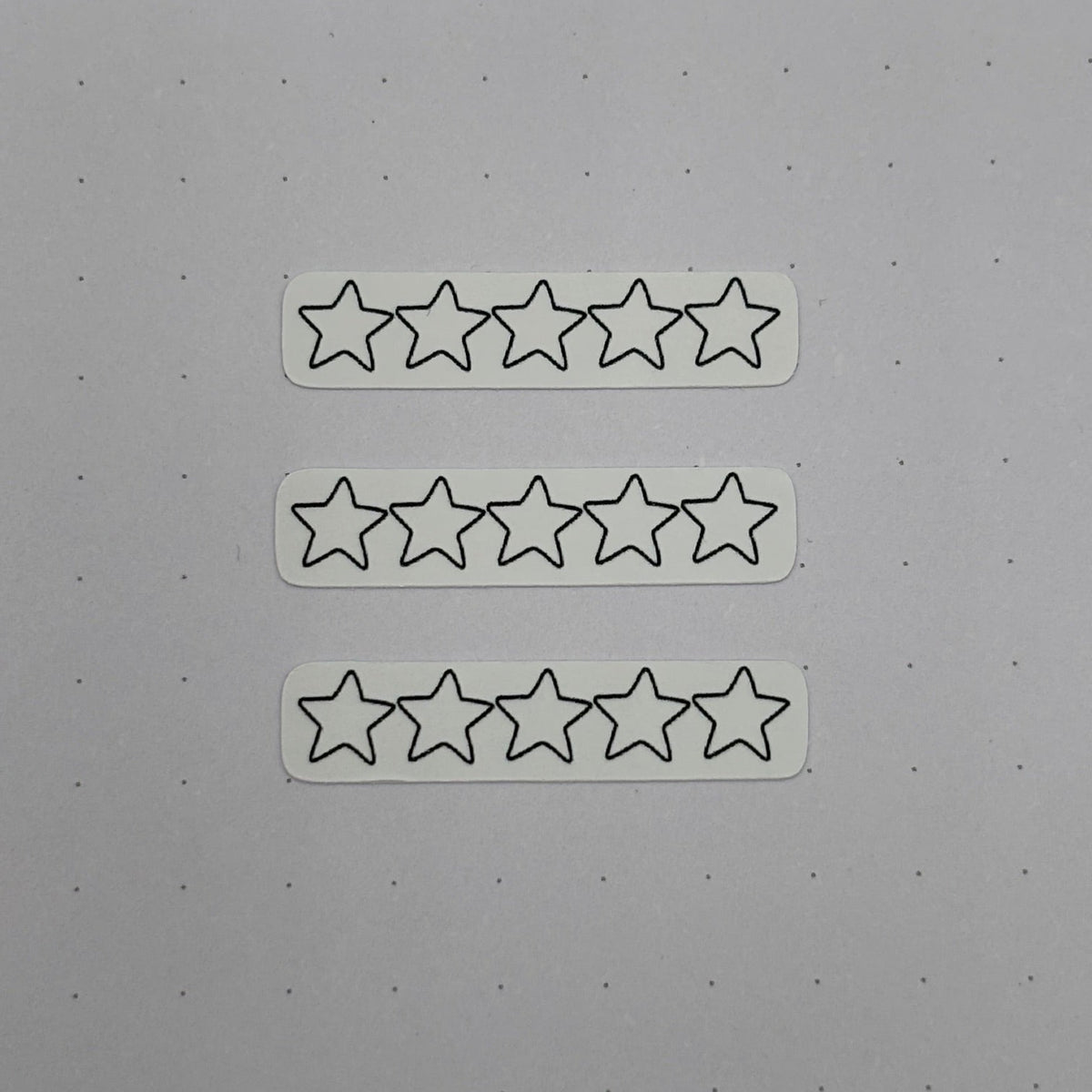 Three white rectangular stickers, each printed with five outlined star icons, arranged vertically on a light gray surface.